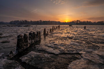 Wall Mural - remains of an old pier over a frozen river during a beautiful sunrise