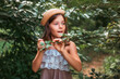 © _KUBE_ - Portrait of pretty amazement little girl in a straw hat holding a magnifier. Tropics forest on the background. The concept of curious childhood, scouting and children's education
