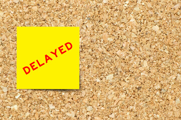 Sticker - Yellow note paper with word delayed on cork board background with copy space