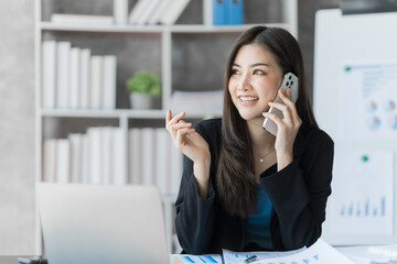 Call mobile, using laptop, Beautiful Asian female bookkeeper doing online accounting with laptop in private accounting office, balance sheet and stock market statistics.