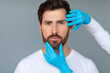© Prostock-studio - Plastic surgery and aesthetic cosmetology concept. Cosmetician hands in protective medical gloves touching male face