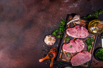 Wall Mural - Raw pork steaks cooking background. Three tasty raw fresh meat steaks with herbs, salt, pepper, olive oil, ready for dinner preparation, dark brown kitchen background copy space