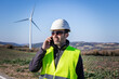© ADDICTIVE STOCK - Engineer in protective helmet speaking on smartphone against wind turbines