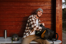 Young Man Tourist Opening Backpack While Sitting On Wooden Bench During Hiking