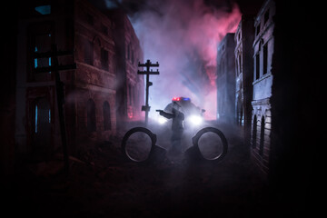 Wall Mural - Police raid at night and you are under arrest concept. Silhouette of handcuffs with police car on backside. Image with the flashing red and blue police lights at foggy background. Slider shot