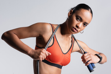 Wall Mural - brunette african american sportswoman in red sports bra holding skipping rope isolated on grey.