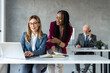 © Dorde - Young businesswoman mentor standing next to executive female manager in glasses negotiating growth business plan at office table, using laptop. Multicultural team work together in office.