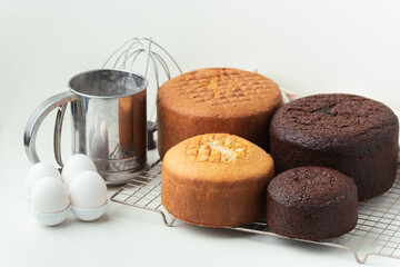 Poster - Freshly baked sponge biscuit on a pastry grid next to whisk, sieve for sifting flour and eggs. Brown chocolate and white vanilla sponge cake with professional confectioner utensils. White background