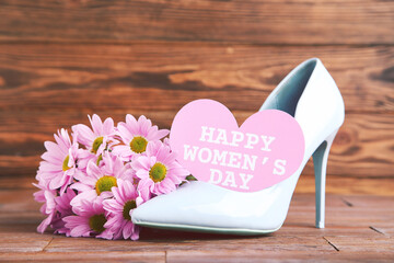 Wall Mural - Flowers of chrysanthemums, card in shape of heart with text Happy Womens Day and blue high-heeled shoe on brown wooden background