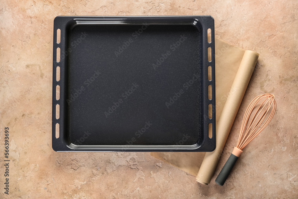 Baking tray with parchment paper and whisk on grunge background