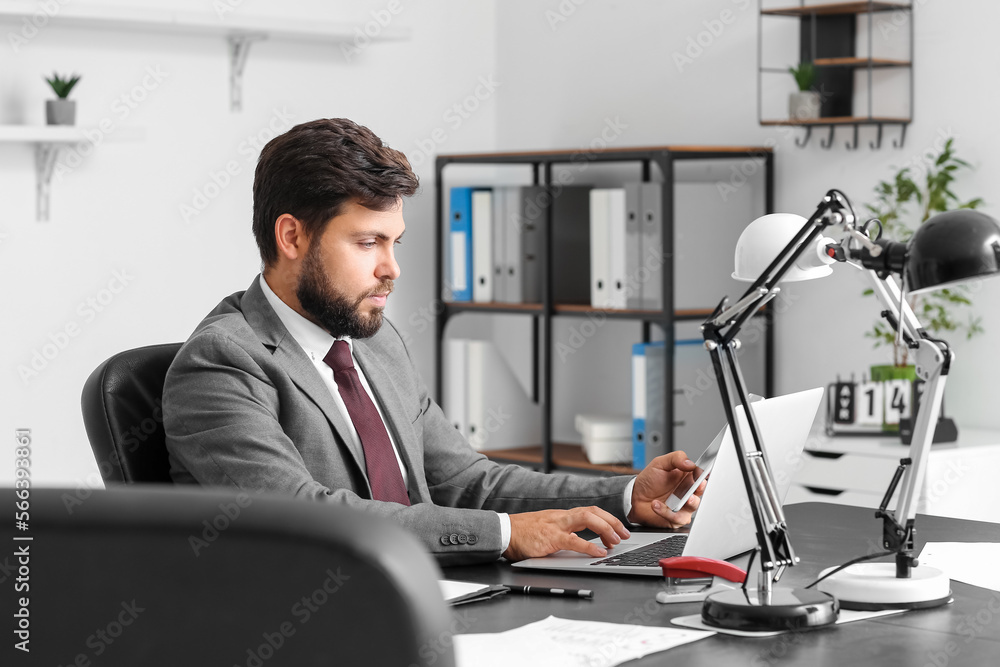 Handsome young businessman working with tablet computer and laptop at table in office