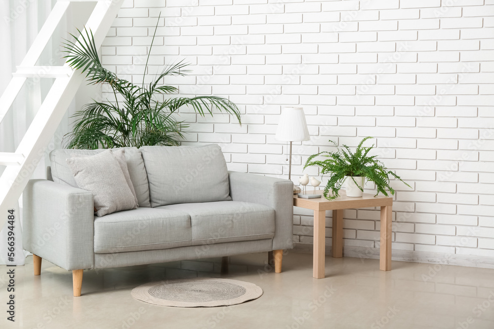 Table with lamp, houseplants and grey sofa in light living room