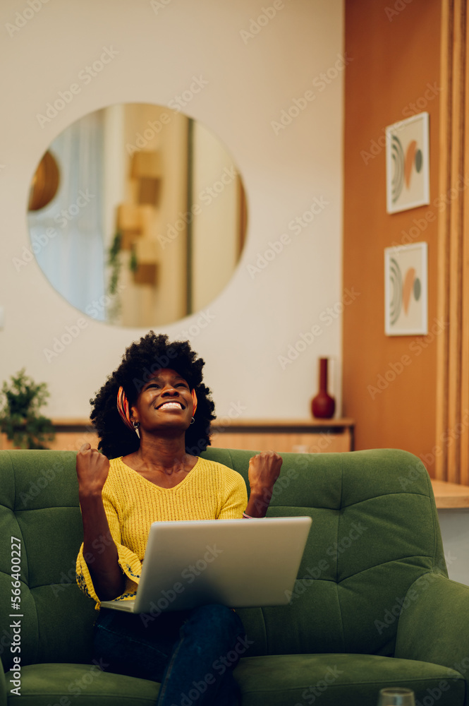 Happy african american woman using laptop while sitting on a couch at ...