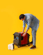 © Pixel-Shot - Young man with portable gasoline generator and electric fan heater on yellow background