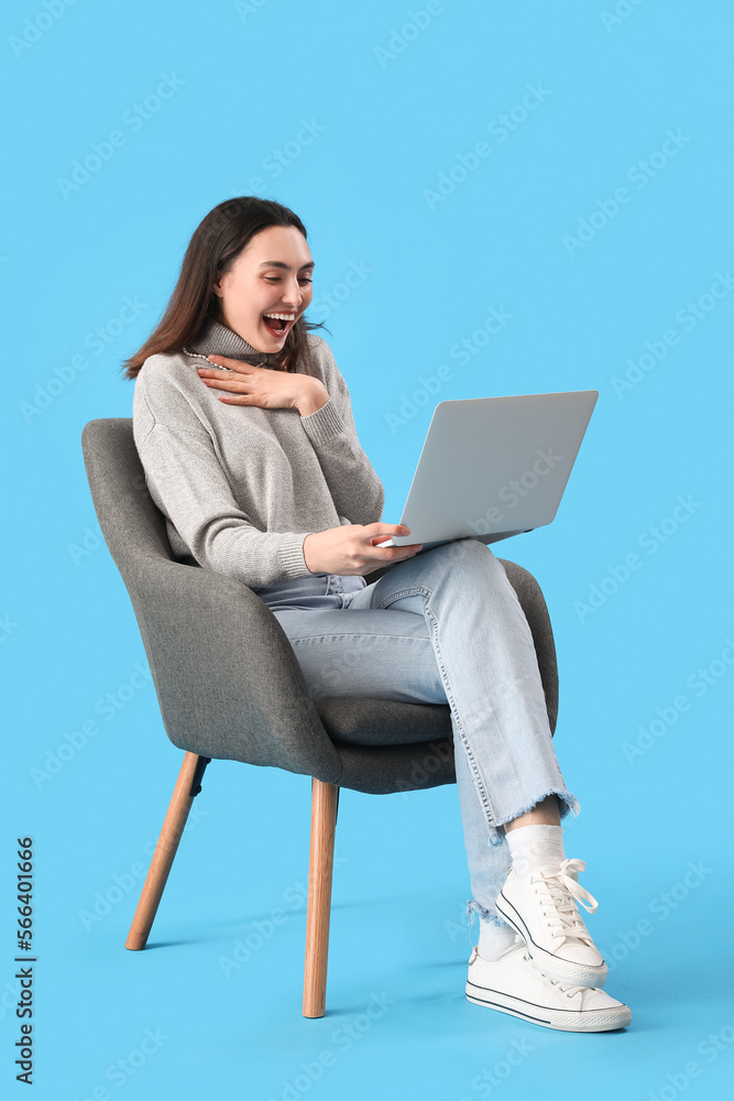 Young woman using laptop in black armchair on blue background