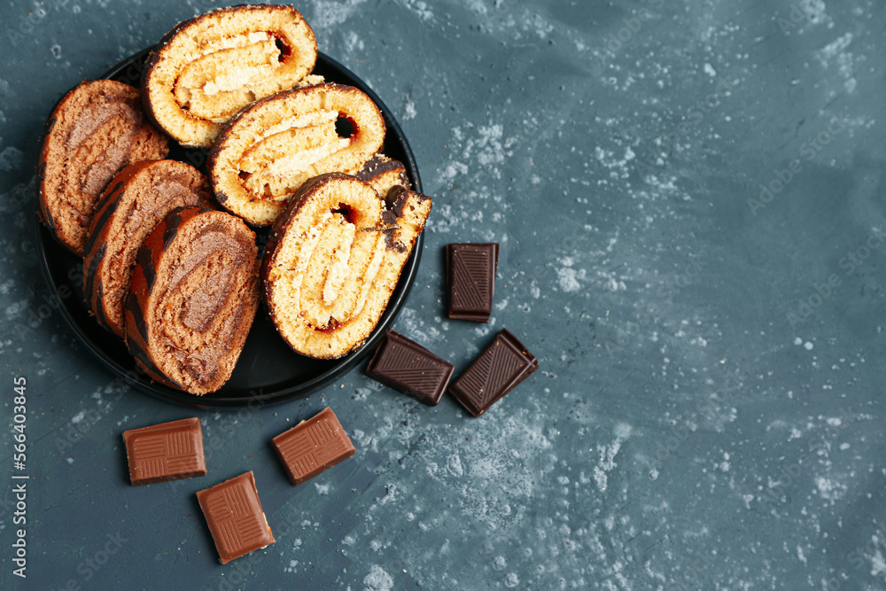 Plate with pieces of delicious sponge cake roll and chocolate on table