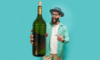 © San4ezz007 - Young bearded charismatic hipster somilier showing a big bottle of wine, isolated on a blue studio background. Wine presentation.
