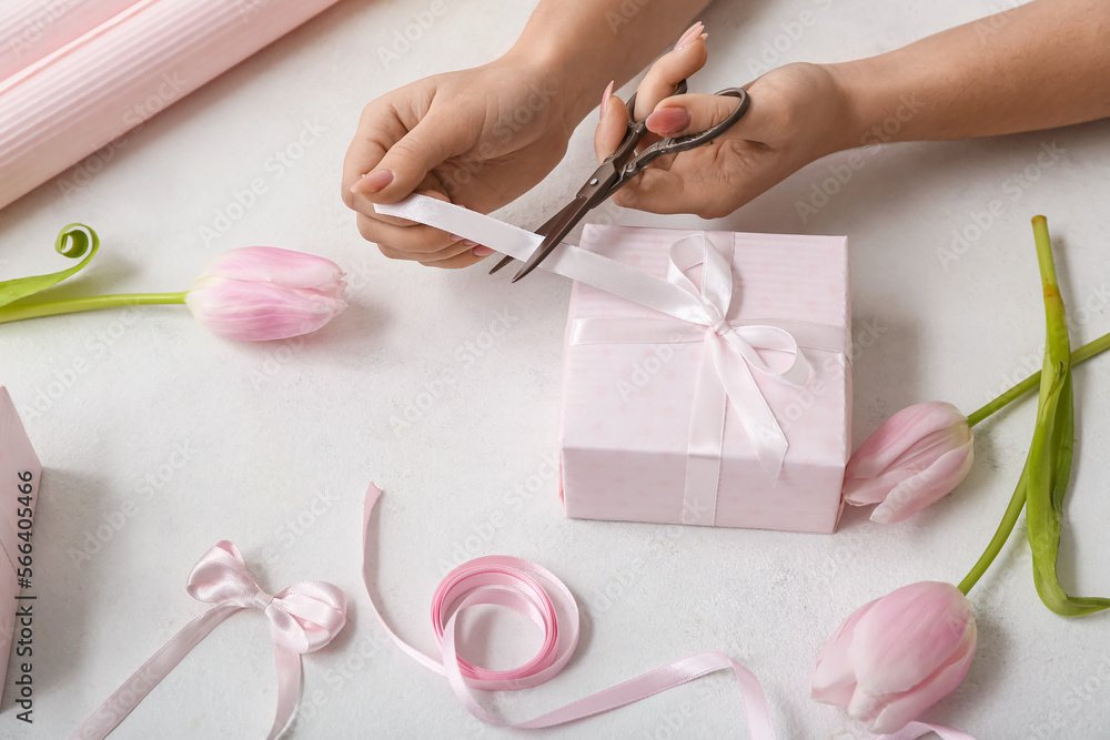 Female hands with beautiful gift box, scissors and tulip flowers on light background. Women's Day celebration