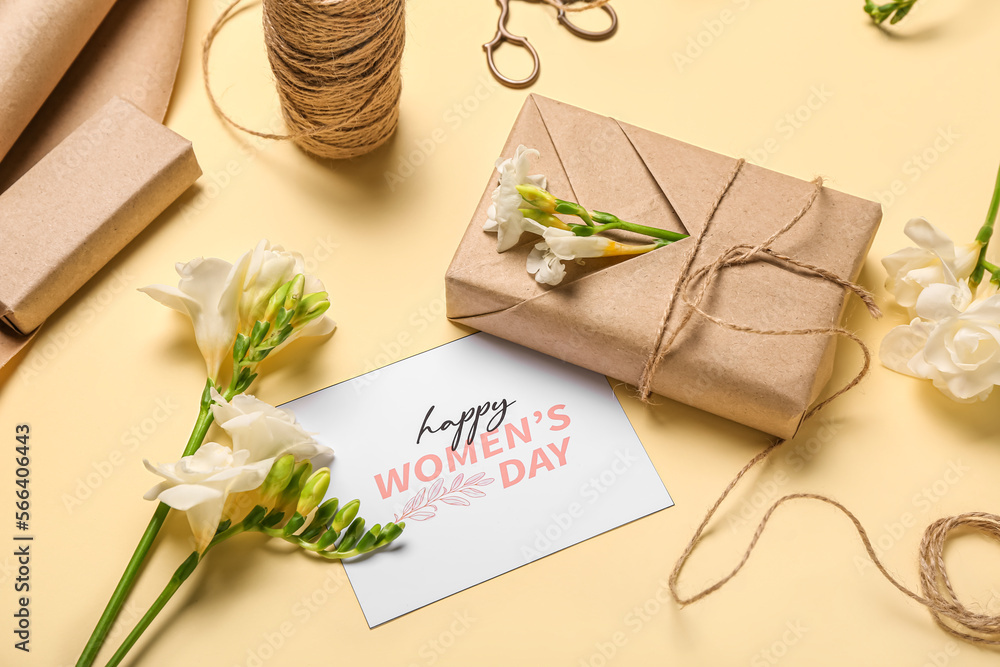 Composition with gift boxes, greeting card, packing materials and freesia flowers on yellow background. Women's Day celebration