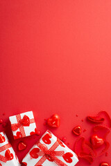 St Valentine's Day concept. Top view vertical photo of gift boxes in wrapping paper with heart pattern ribbon candies candle and sprinkles on isolated red background with copyspace