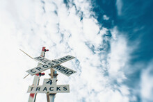 Low Angle View Of Railroad Track And Crossing Sign Against Cloudy Sky
