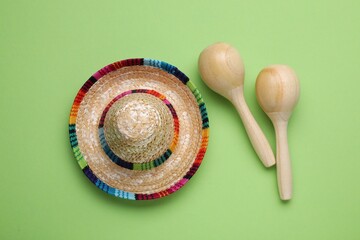 Colorful maracas and sombrero hat on light green background, flat lay. Musical instrument