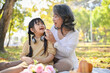 © bongkarn - Happy and caring Asian grandmother feeding doughnut to her little granddaughter while picnicking