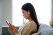 © Monster Ztudio - Happy young asian woman relax on comfortable couch at home texting messaging on smartphone, smiling girl use cellphone chatting, browse wireless internet on gadget, shopping online from home