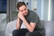 © Евгений Шемякин - Sad upset depressed unhealthy guy, young tired exhausted frustrated man is suffering at home, sitting on couch or sofa, having headache, migraine. Failure, despair, depression concept
