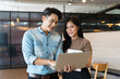 © amorn - Asian business man and woman standing discuss and working with laptop computer at the office workspace. Two Asian colleagues man and woman discussing or brainstorming together in the modern office