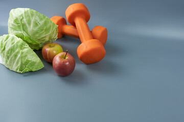 Red apples and kale and fitness dumbbells on a gray background. The concept is a meal plan for workouts. 