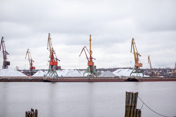 Poster - River port in winter. Port cranes on the bank of the river. Embankment of the river port, a barge at the quay wall. Large port cranes on the river. Extraction and transportation of sand other cargo
