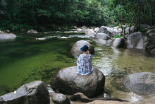 Woman Sitting On Rock In The Lush Rainforest Of Mossman Gorge In Far North Queensland.