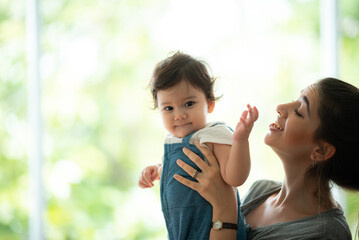 Wall Mural - Cute little baby toddler playing and enjoying while in the arms of young mother hugging at home