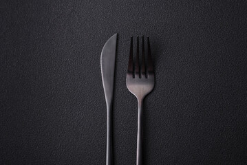 Metal kitchen knife and fork on a dark textured concrete background