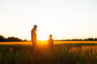 © Acronym - Farmer and his son in front of a sunset agricultural landscape. Man and a boy in a countryside field. Fatherhood, country life, farming and country lifestyle concept.