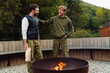 © Drobot Dean - Two white man smiling and talking while standing by campfire in forest