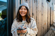 © Drobot Dean - Young asian woman smiling and using cellphone while standing outdoors