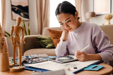 Young beautiful woman artist drawing on digital tablet while sitting at table