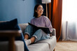 © Drobot Dean - Smiling asian woman reading book while sitting on couch
