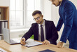 © Studio Romantic - Business people working with a contract in the office. Team of two young men in formal suits reading the terms and conditions of a professional business contract agreement before signing it