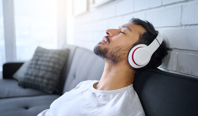 Sticker - Relax, music and man with headphones on sofa in home living room streaming radio or podcast. Meditation, technology and male on couch in lounge listening to peaceful song, audio or album in house.