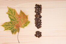 Exclamation Mark. An Exclamation Mark Collected From Roasted Coffee Beans Lies On A Wooden Tabletop. Nearby Lies A Maple Autumn Leaf