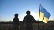 Ukrainian army soldiers stands outdoor at sunset time and waves flag of Ukraine. People in military uniform lifted up flag against blue sky. Victory at war. Resistance to russian invasion. Slow motion