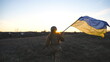Female ukrainian army soldier runs and waves flag of Ukraine at sunset. Woman in military uniform lifted up flag in honor of the victory against russian aggression. Invasion resistance concept. Slowmo