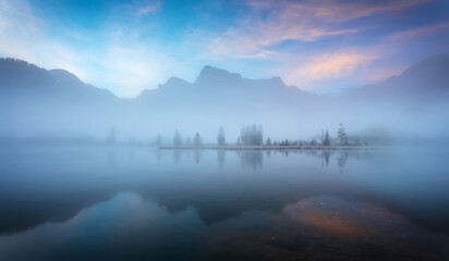 Fotobehang - Fabulous misty morning scene of nature. View of Forest lake, Almsee lake in highland with rocky peak on background. Stunning wild nature during sunrise. Amazing natural summer scenery Creative image.