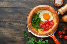 Dutch Baby Pancake. Fresh Homemade Dutch Baby Pancake With Fried Egg, Tomato And Green Arugula In Reed Cast-iron Pan On Old Wooden Table. Flat Lay, Close Up.