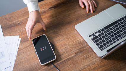 Wall Mural - Charging mobile phone battery with wireless charging device in the table. Smartphone charging on a charging pad. Mobile phone near wireless charger Modern lifestyle technology concept.