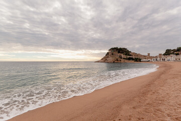 Panorámica de la playa de Tossa de Mar en Girona con el castillo sobre la montaña en el fondo bajo un cielo especial con nubes.