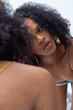 © Beatriz - Mujer joven latina con el pelo rizado y un vestido de tirantes de varios colores posando delante de un espejo con el fondo una pared blanca.